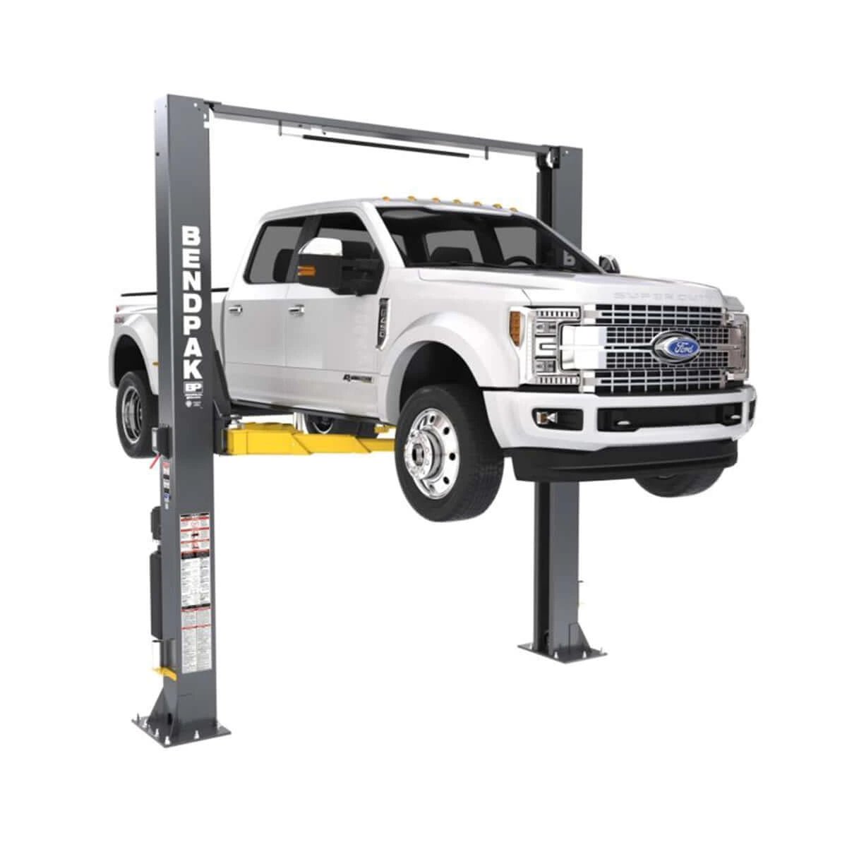 BendPak 12APX two-post lift raising a white pickup truck, front angle view.