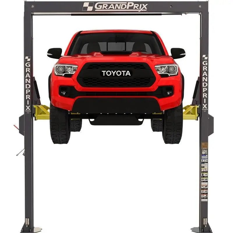 BendPak GP-7 two-post lift raising a red pickup, front view showing GrandPrix-branded gray columns, overhead crossbar, and yellow telescoping arms.