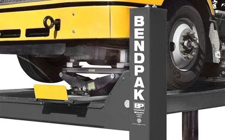 Side view of BendPak HDS-27X four-post lift with heavy-duty rolling bridge jack lifting a yellow commercial truck axle, showing reinforced steel columns and runway structure.