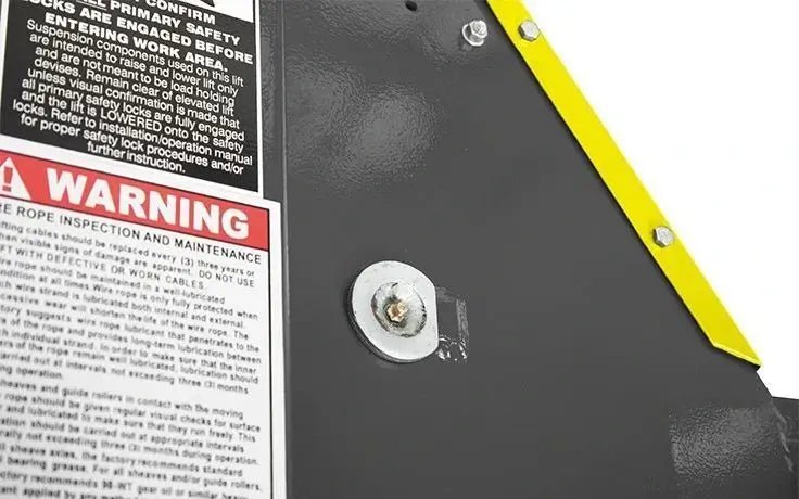 Close-up view of BendPak HDS four-post lift carriage assembly showing steel plate, yellow safety edge guard, and warning label about rope inspection and maintenance.