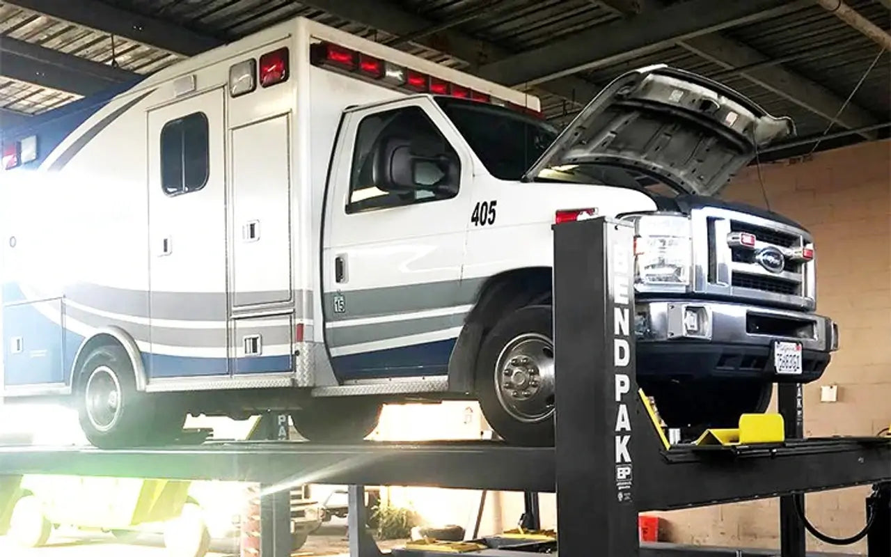 BendPak HDS-14X four-post lift supporting an ambulance in service bay, highlighting commercial-duty capacity and open-front design.