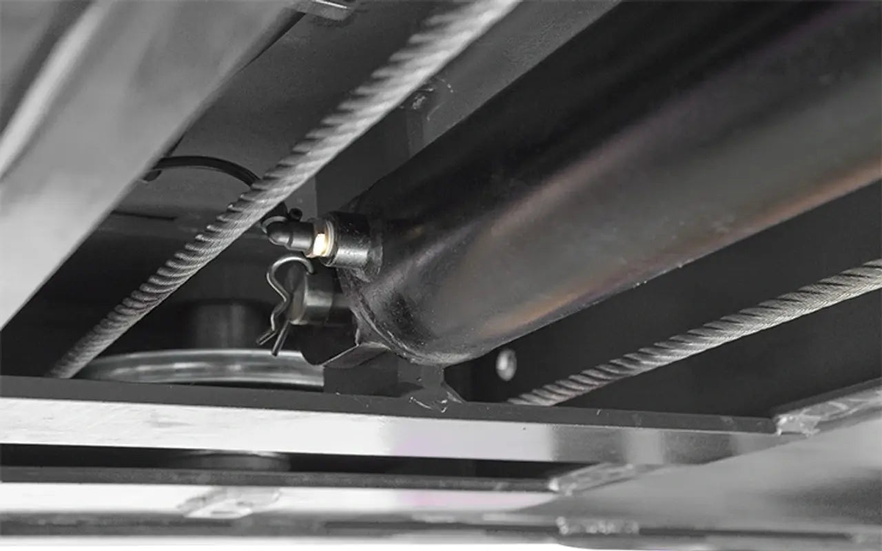 BendPak HDS-14X four-post lift closeup of hydraulic cylinder and steel lift cables, underside view showing locking pin mechanism.