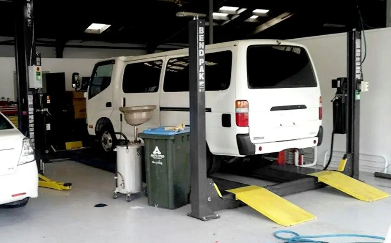 BendPak HDS-14X four-post lift in workshop lifting a white service van, showing yellow ramps and high-clearance structure for undercar access.