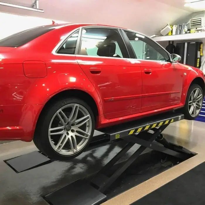 BendPak SP-7XEF full-rise scissor lift installed in home garage raising a red sedan; example of flush-mount configuration for compact service spaces.
