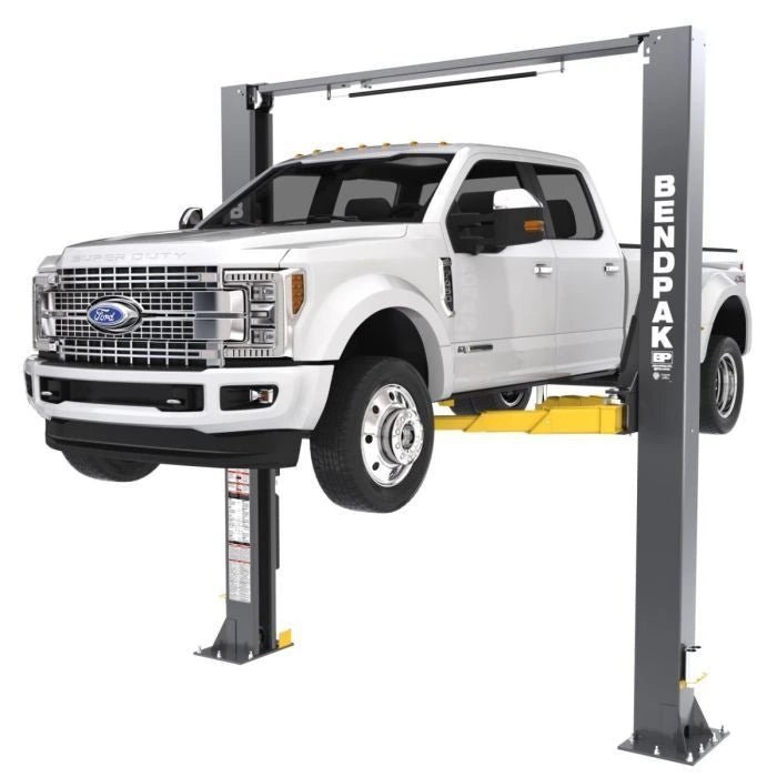 BendPak XPR-12CL two-post lift lifting a Ford Super Duty truck; front-right angle emphasizing clearfloor design and equalized column structure.