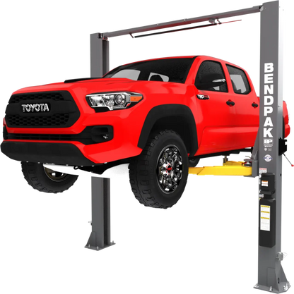 BendPak 10APX two-post lift in hero view raising a red Toyota pickup, clearfloor design with overhead beam, Low-Pro arms and column power unit.
