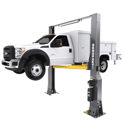 BendPak 16AP two-post lift raising a white service truck, side angle showing heavy-duty construction, yellow lifting arms, and gray steel columns with BendPak logo.