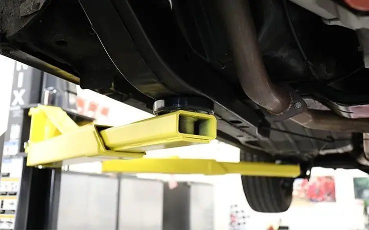 BendPak GP-7 two-post lift closeup showing yellow low-profile arms positioned under a vehicle frame, highlighting clearance and arm design for easy access.