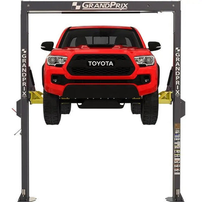 BendPak GP-7 two-post lift raising a red pickup, front view showing GrandPrix-branded gray columns, overhead crossbar, and yellow telescoping arms.