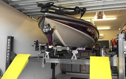 BendPak HD-7500BLX extended-length four-post lift installed in a home garage, lifting a Javelin bass boat and trailer on yellow steel ramps, showcasing its marine storage capability and heavy-duty design.
