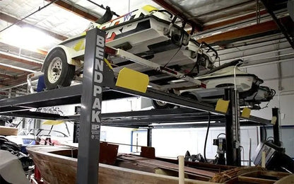 BendPak HD-7500BLX extended-length four-post lift installed in a garage, holding a classic car on the upper platform with visible yellow ramps and BENDPAK-branded steel columns in a workshop setting