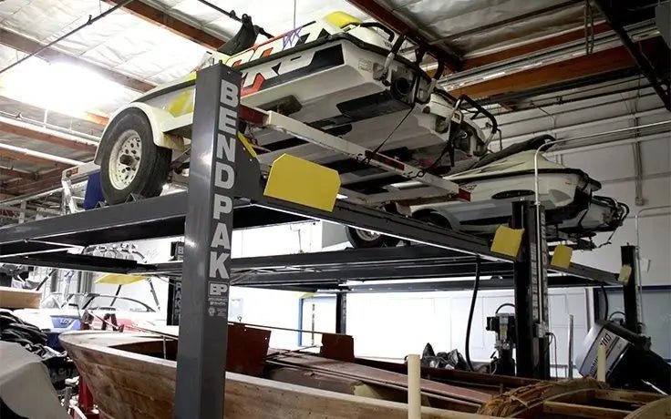 BendPak HD-7500BLX extended-length four-post lift installed in a garage, holding a classic car on the upper platform with visible yellow ramps and BENDPAK-branded steel columns in a workshop setting