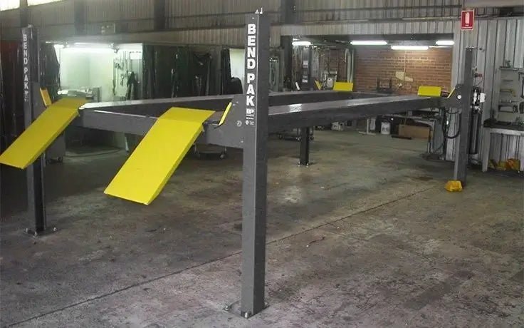 BendPak HD-9STX four-post lift installed in an auto shop showing full assembly with yellow ramps, tall columns, and extended-height runways for vehicle storage or service.