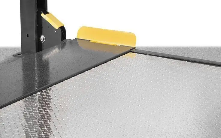 BendPak HD-9SWX four-post lift closeup of aluminum solid deck platform showing diamond-plate surface, yellow wheel stops, and column corner connection for parking stability.