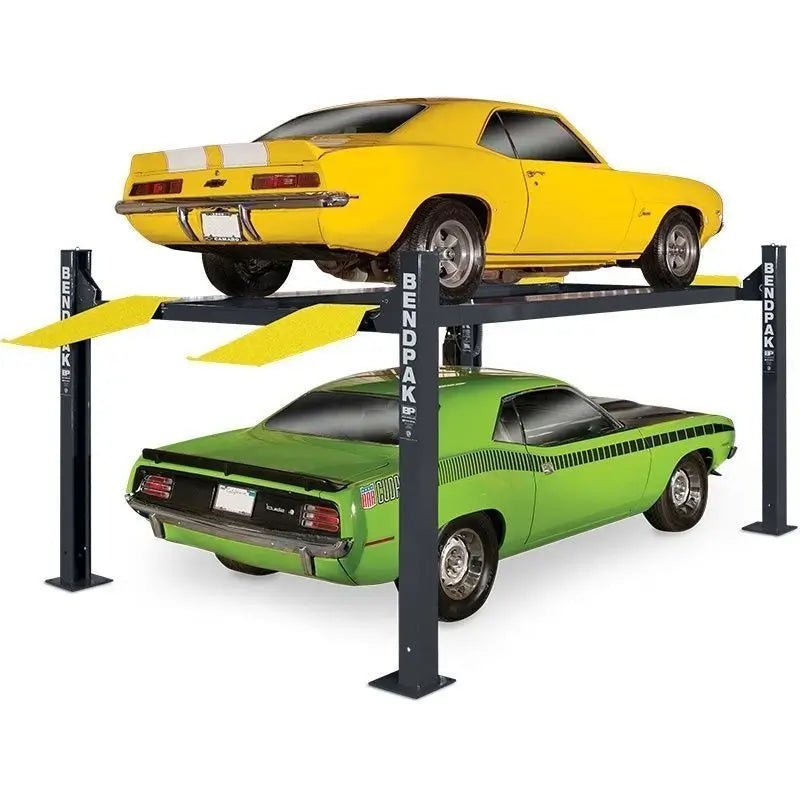 BendPak HD-9XL four-post lift with a yellow muscle car elevated above a green car, showing the extended runways, yellow drive-on ramps, and heavy-duty steel columns for vehicle storage or maintenance.