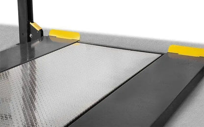 BendPak HD-9XW four-post lift closeup showing optional aluminum solid deck platform with diamond-plate surface and yellow wheel stops for full vehicle support.
