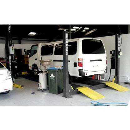 BendPak HDS-14 four-post lift in automotive workshop lifting a white van, showing open-front access and integrated hydraulic operation.