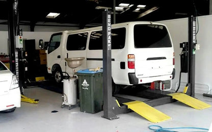 BendPak HDS-14X four-post lift in workshop lifting a white service van, showing yellow ramps and high-clearance structure for undercar access.