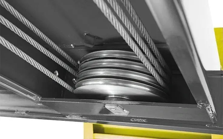 Underside view of BendPak heavy-duty four-post lift showing large precision cable sheaves and steel cables that reduce wear and ensure balanced lifting motion.
