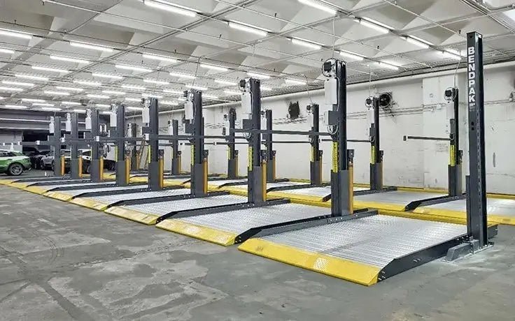 BendPak PL-6000DC two-post parking lifts arranged in a commercial storage bay; metal platforms with yellow edges under bright overhead lighting.