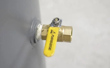 Close-up of the brass outlet valve on a BendPak VMP-7580V-601 V-Max Patriot air compressor tank, showing yellow Airbase handle and threaded brass fitting against gray steel surface.