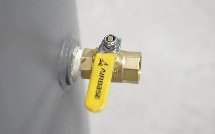 Close-up of the brass outlet valve on a BendPak VMP-7580V-601 V-Max Patriot air compressor tank, showing yellow Airbase handle and threaded brass fitting against gray steel surface.