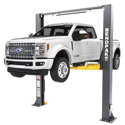 BendPak XPR-12CL two-post lift lifting a Ford Super Duty truck; front-right angle emphasizing clearfloor design and equalized column structure.