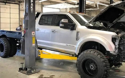 BendPak XPR-18CL two-post lift supporting a Ford Super Duty in a garage; side view showing asymmetrical arm setup and extended truck clearance