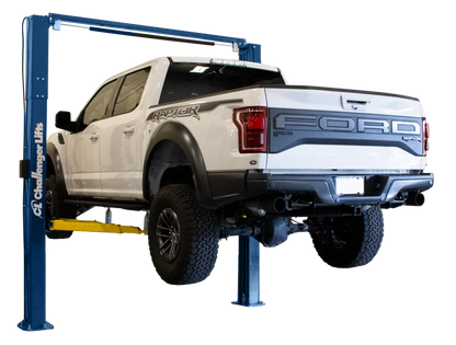 Challenger VLE10 two post lift raising a white Ford Raptor pickup, demonstrating heavy duty 10000 lb lifting capacity and dual position arm design for trucks