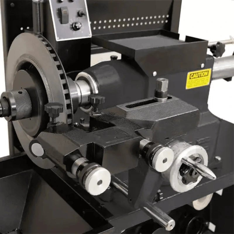 Katool RL-8500 brake lathe closeup showing twin cutting head assembly with adjustment knobs, rotor mount, tool holder, and visible caution label on the housing.